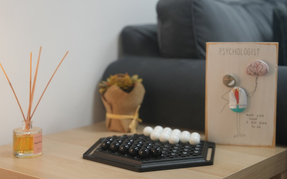 Detalle de la mesa de la sala de Jokabide: un difusor de varillas, un ramo seco envuelto en papel, un juego de canicas y una tarjeta de madera con un psicólogo dibujado