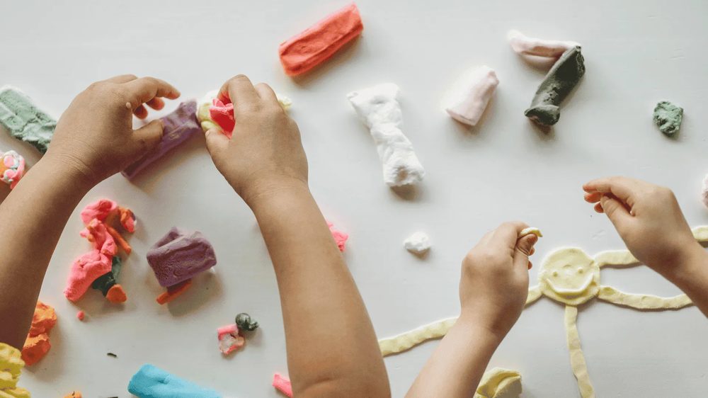 Las manos de dos niños modelando figuras de plastilina de colores sobre una mesa