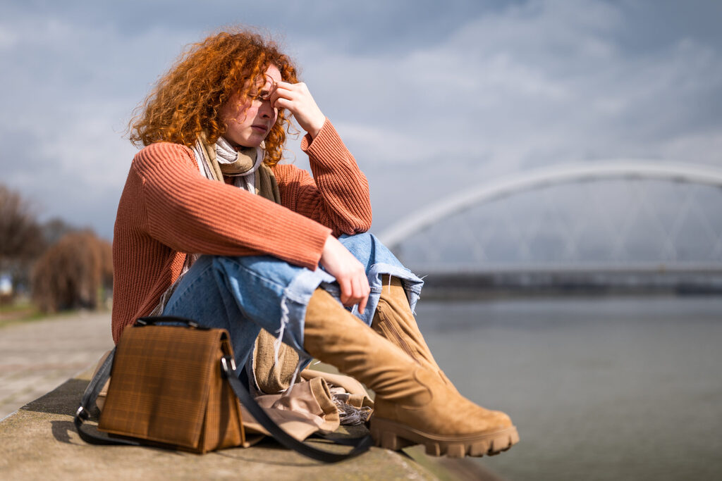 Una mujer sentada junto al río, con la mano en la frente