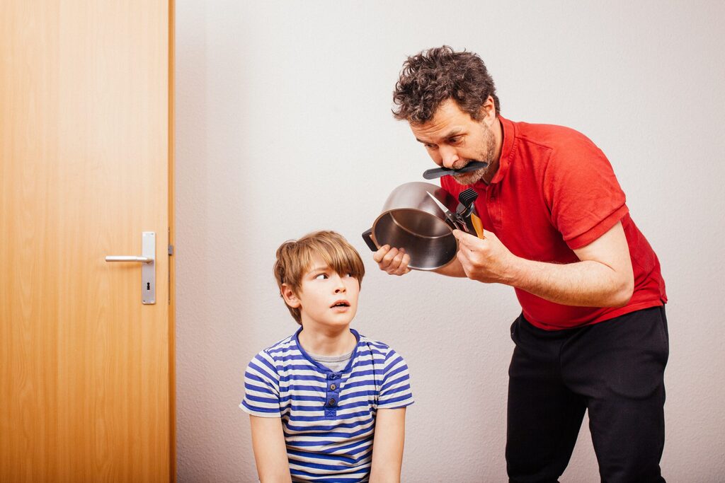 Un padre se acerca a su hijo con un cazo y unas tijeras para cortarle el pelo
