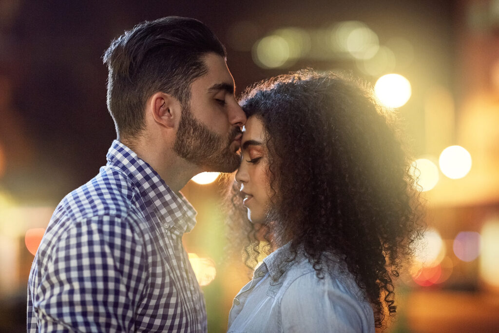 Una pareja de noche en la calle: él le da un beso en la frente