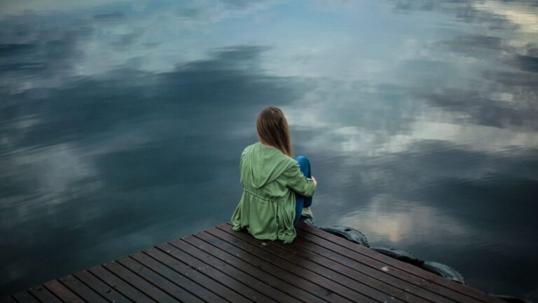 mujer en un muelle mirando a un lago, reflexionando sobre su crisis vital